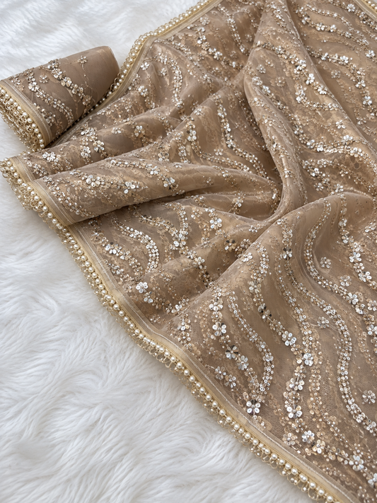 Golden Net Saree for Women, Pearl and Sequin Embroidered Designer Saree.A beige embellished dupatta or scarf with intricate silver and gold sequin patterns and a beaded border, draped on a white faux fur surface.