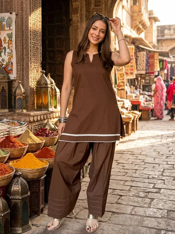 A woman modeling a brown sleeveless Farshi kurta and wide-leg salwar pants set with a thin white stripe detail,