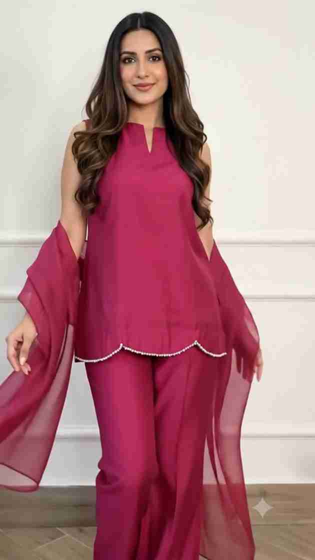 A woman modeling a magenta pink two-piece traditional outfit with a sleeveless top, matching wide-leg pants, and sheer draped sleeves