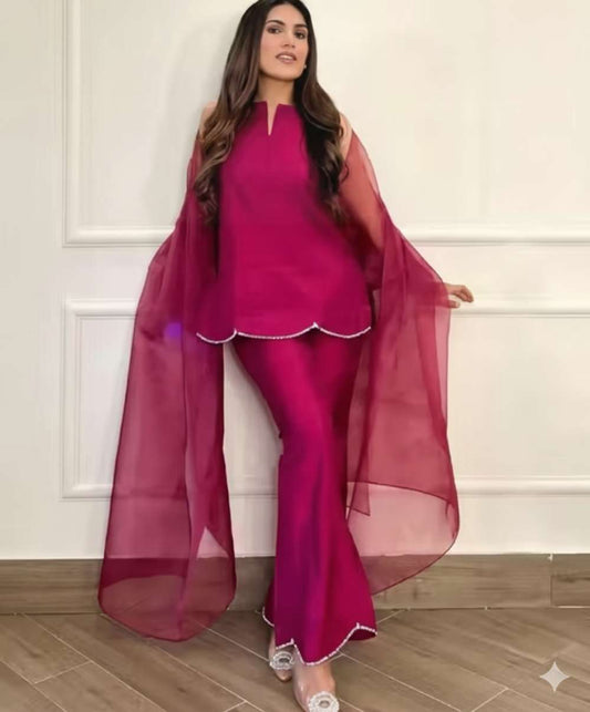 A woman modeling a magenta pink traditional outfit consisting of a sleeveless kurta with a scalloped hem, matching flared pants, and a sheer matching dupatta,