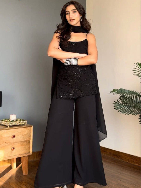 A woman models a black sleeveless halter-neck Kurti with a matching sheer draped cape and wide-leg Sharara