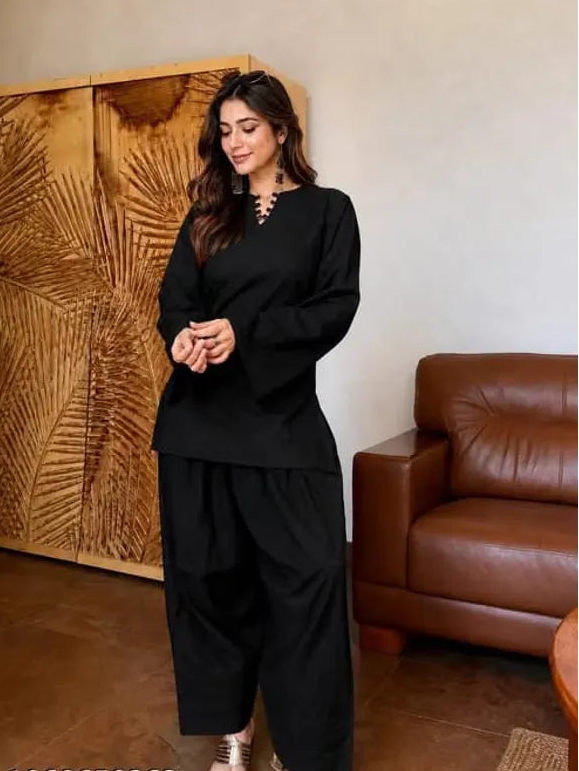 A woman modeling a black two-piece Farshi Suit outfit consisting of a long-sleeve top with a split neckline and matching wide-leg pants, 