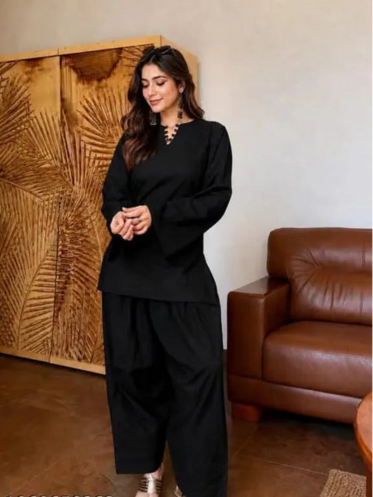 A woman modeling a black two-piece Farshi Suit outfit consisting of a long-sleeve top with a split neckline and matching wide-leg pants, 