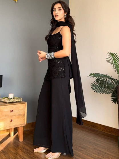 A woman models a black traditional outfit consisting of a sleeveless embellished Kurta, wide-leg Sharara, and a matching draped scarf