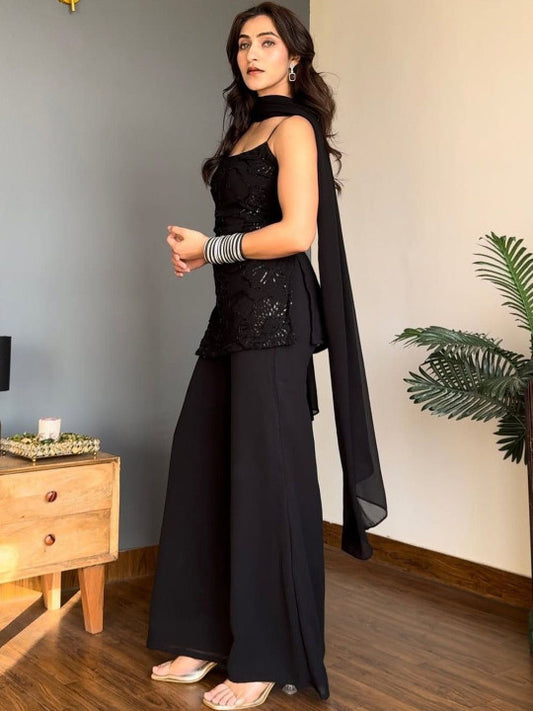 A woman models a black traditional outfit consisting of a sleeveless embellished Kurta, wide-leg Sharara, and a matching draped scarf