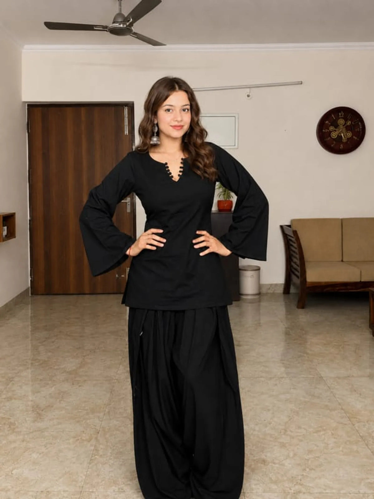 A woman modeling a black traditional Farshi Suit outfit with a long-sleeved tunic Kurta and wide-leg Farshi pants 