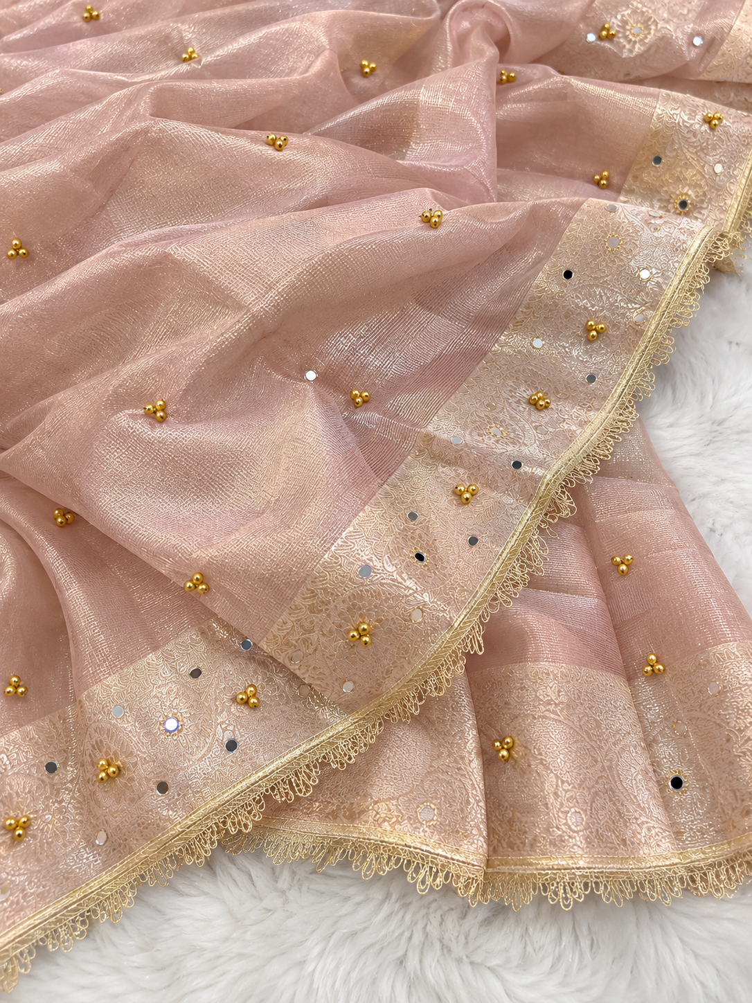 A ghungru sari dusty pink organza saree with gold zari embroidery, gold mirror work, and a decorative border, laid out on a white faux fur surface.