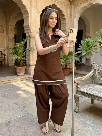 A woman wearing a brown traditional Indian Frashi Suit Salwar outfit with white piping details the fabric is cotton 