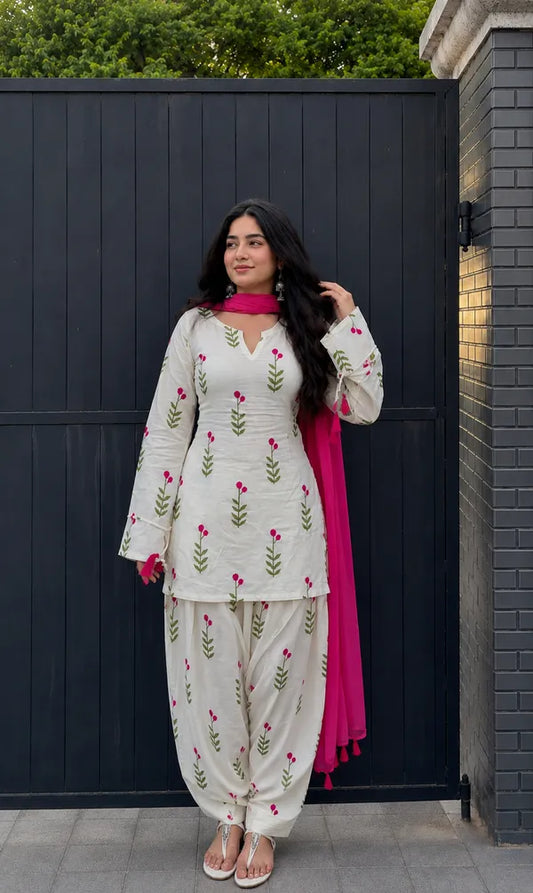 A woman modeling a traditional Indian farshi suit salwar kameez suit with a white base, green leaf embroidery, pink floral motifs, and a bright pink dupatta, 
