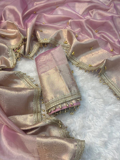 Ghungroo saree A folded pink and gold zari fabric textile with ornate metallic borders and small gold embellishments, arranged on a white faux-fur surface.