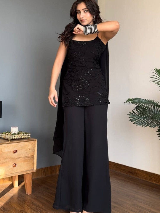 A woman modeling a black sleeveless embellished Kurta with matching wide-leg Sharara and a draped black shawl