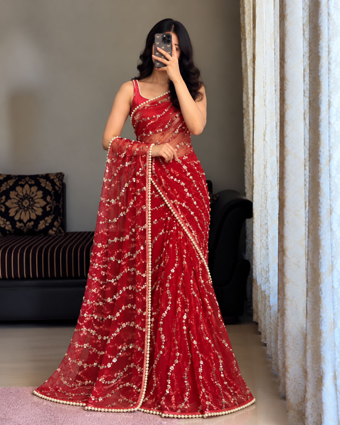 Red Sequin Net saree . Party Wear .A woman wearing a red sleeveless saree with gold sequin embroidery and a gold border, taking a mirror selfie in an indoor setting.