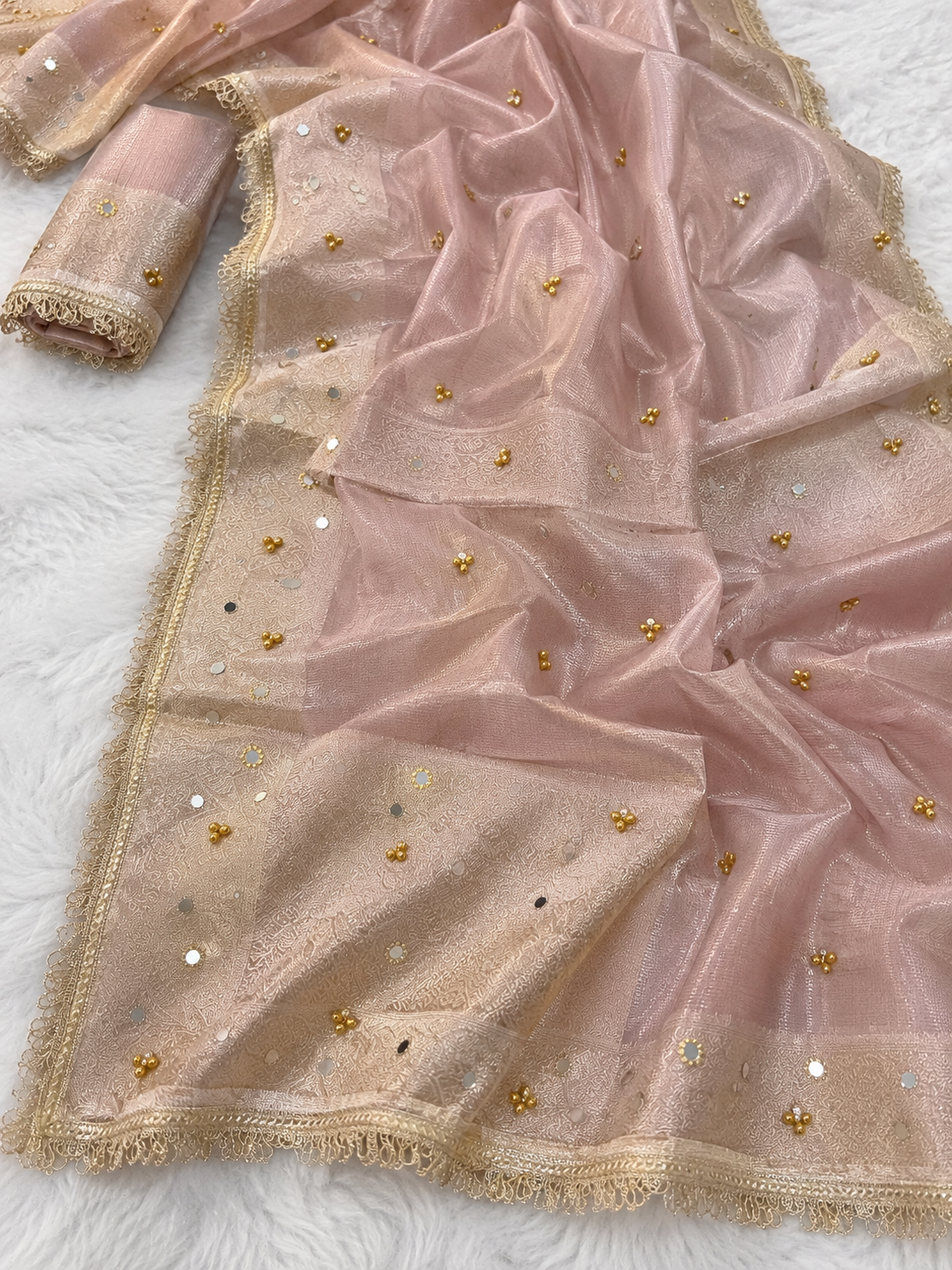 A Ghungroo pink organza saree with gold zari embroidery, gold and silver mirror work, and a matching rolled blouse piece, displayed on a white textured background.