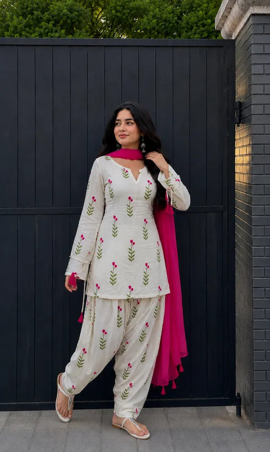 Farshi Suit Salwar A woman modeling a traditional Indian outfit consisting of a cream-colored kurta and pajama set with green and pink floral embroidery, paired with a bright pink dupatta, 