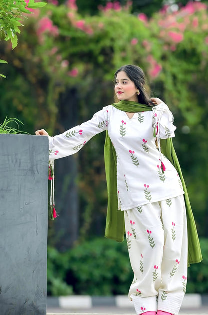 A woman wearing a white traditional Farshi Suit outfit with pink floral embroidery and a green dupatta,
