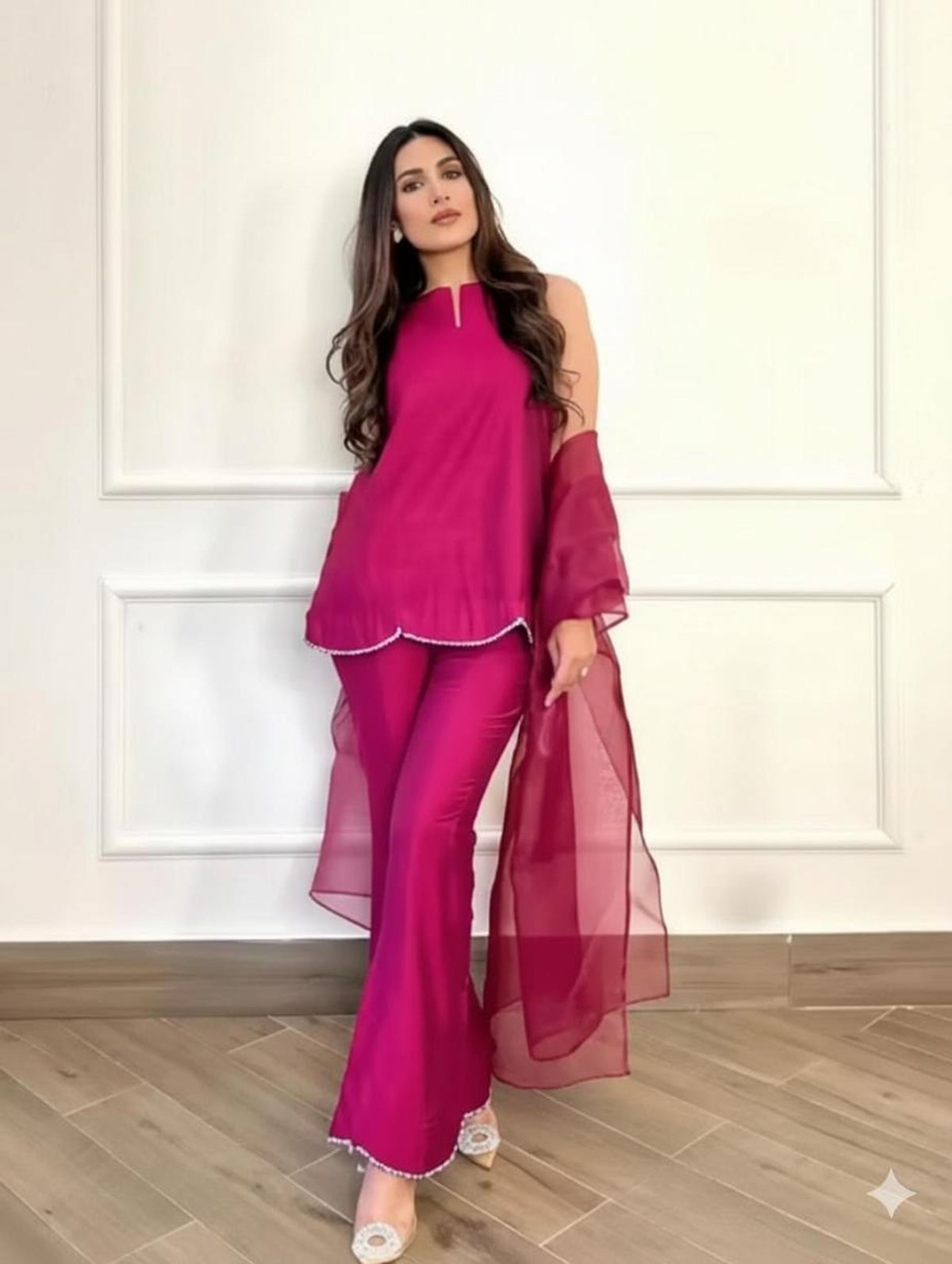 A woman models a bright magenta pink traditional outfit consisting of a sleeveless top with cold-shoulder sleeves, matching flared pants, and a sheer matching dupatta 