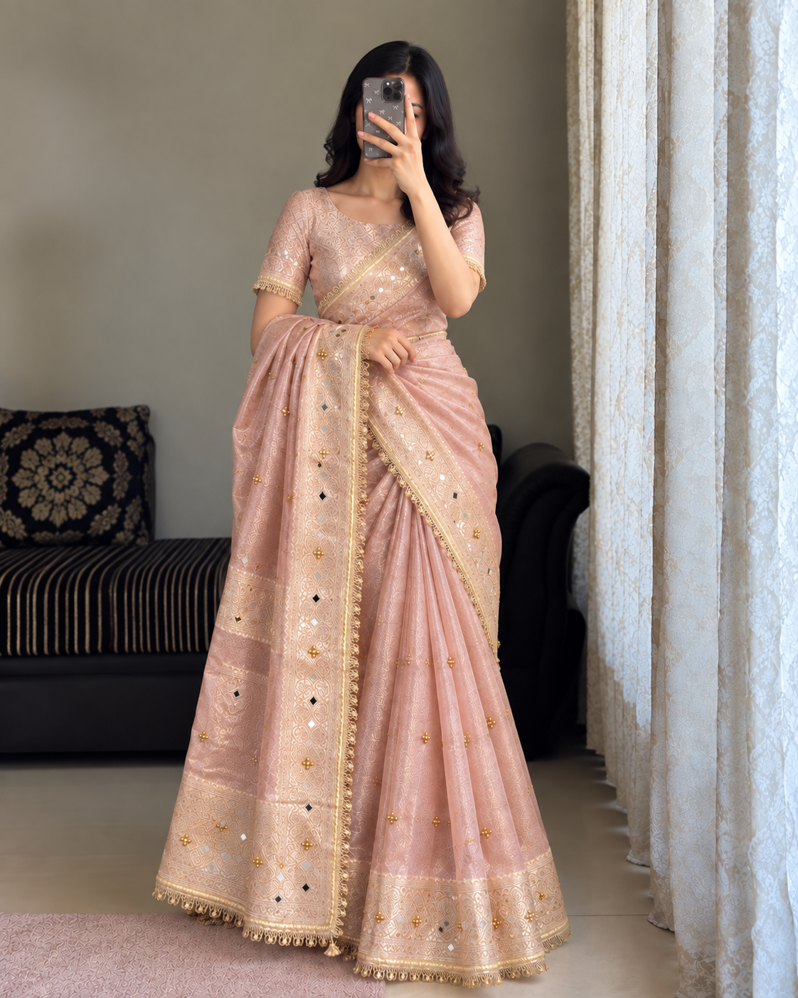 A woman wearing a light pink traditional ghungroo banarasi saree with gold embroidery and mirror work, taking a mirror selfie in an indoor setting.