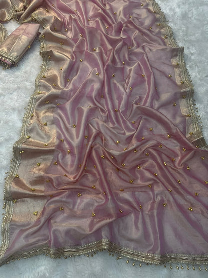A draped dusty rose pink organza fabric with gold zari embroidery and small gold Ghungroo bead embellishments, laid out on a white textured background.