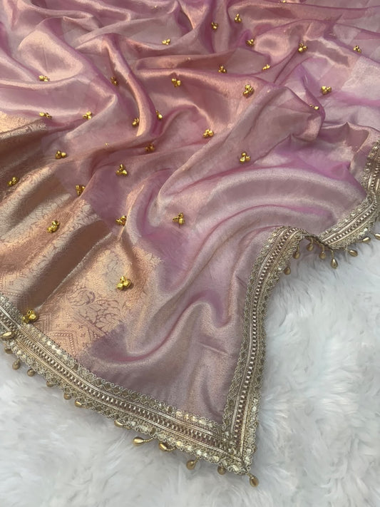 A draped pink Banarasi Soft Tissue Silk with gold zari embroidery and small ghungroo gold bead embellishments, laid flat on a white faux fur surface.